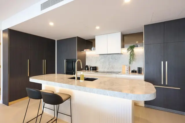 Kitchen with grey marble island, dark timber cabinetry, brass tapware and black bar stools