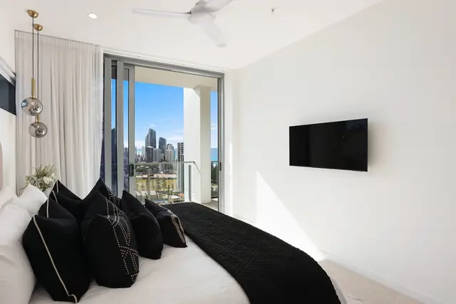 Bedroom with cream scalloped headboard, black cushions and fur throw framing floor-to-ceiling skyline views