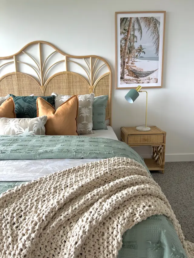 Bedroom with arched rattan bedhead, sage and terracotta cushions and tropical hammock artwork