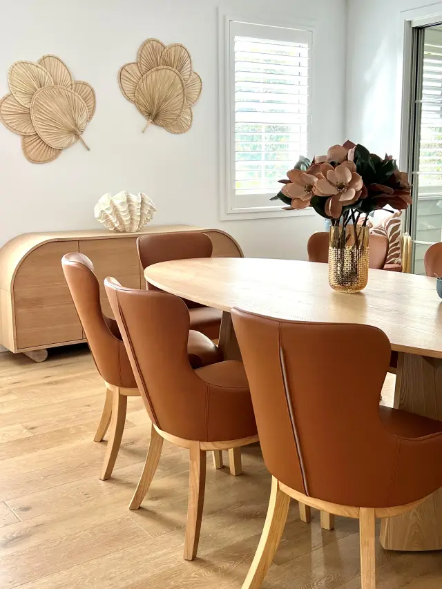 Dining area with oval oak table, tan leather wingback chairs and palm fan wall art