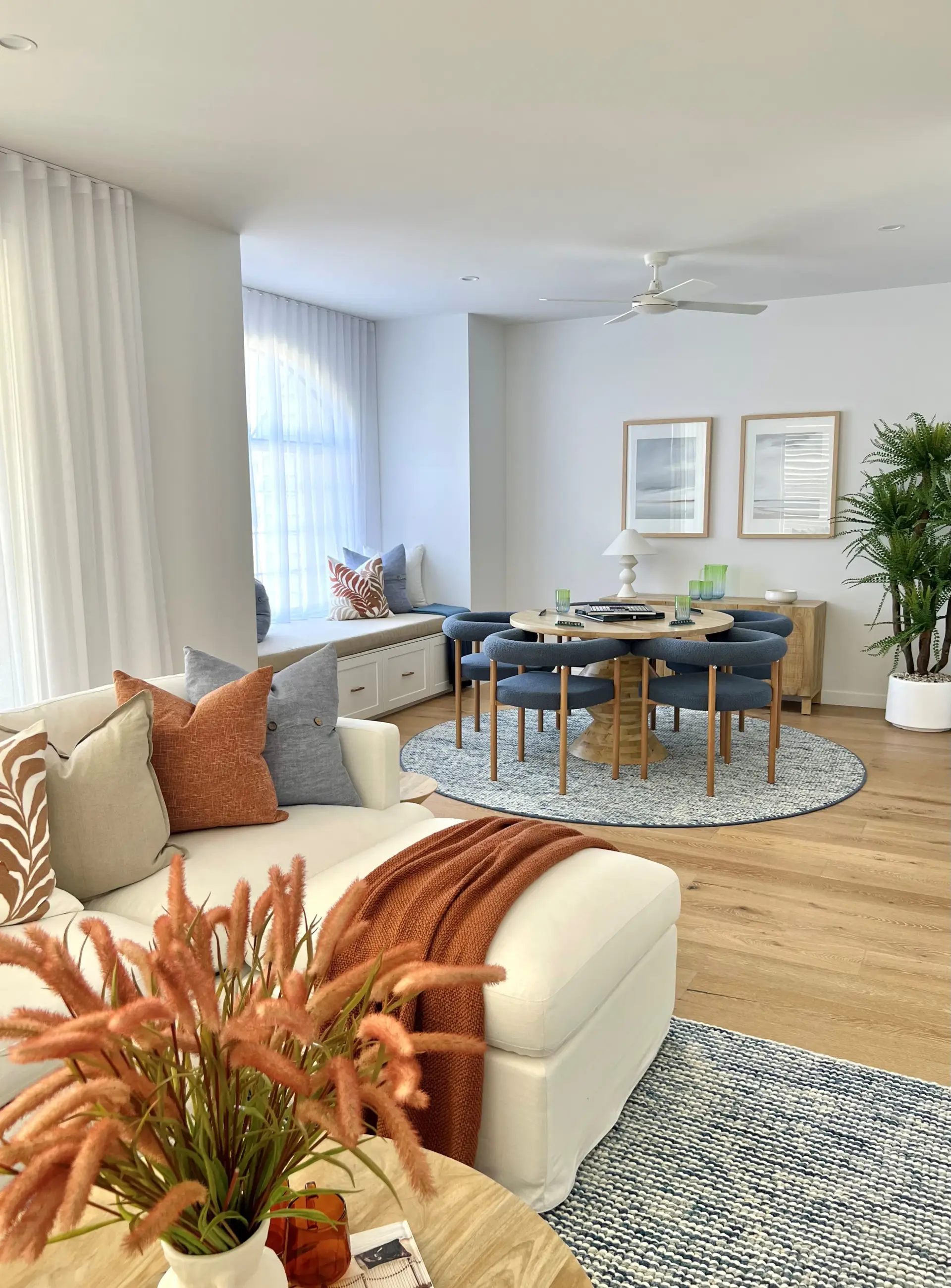 Open-plan family and dining room at Golden Beach with a white linen sofa, built-in window seat and a round timber dining table with blue bouclé chairs