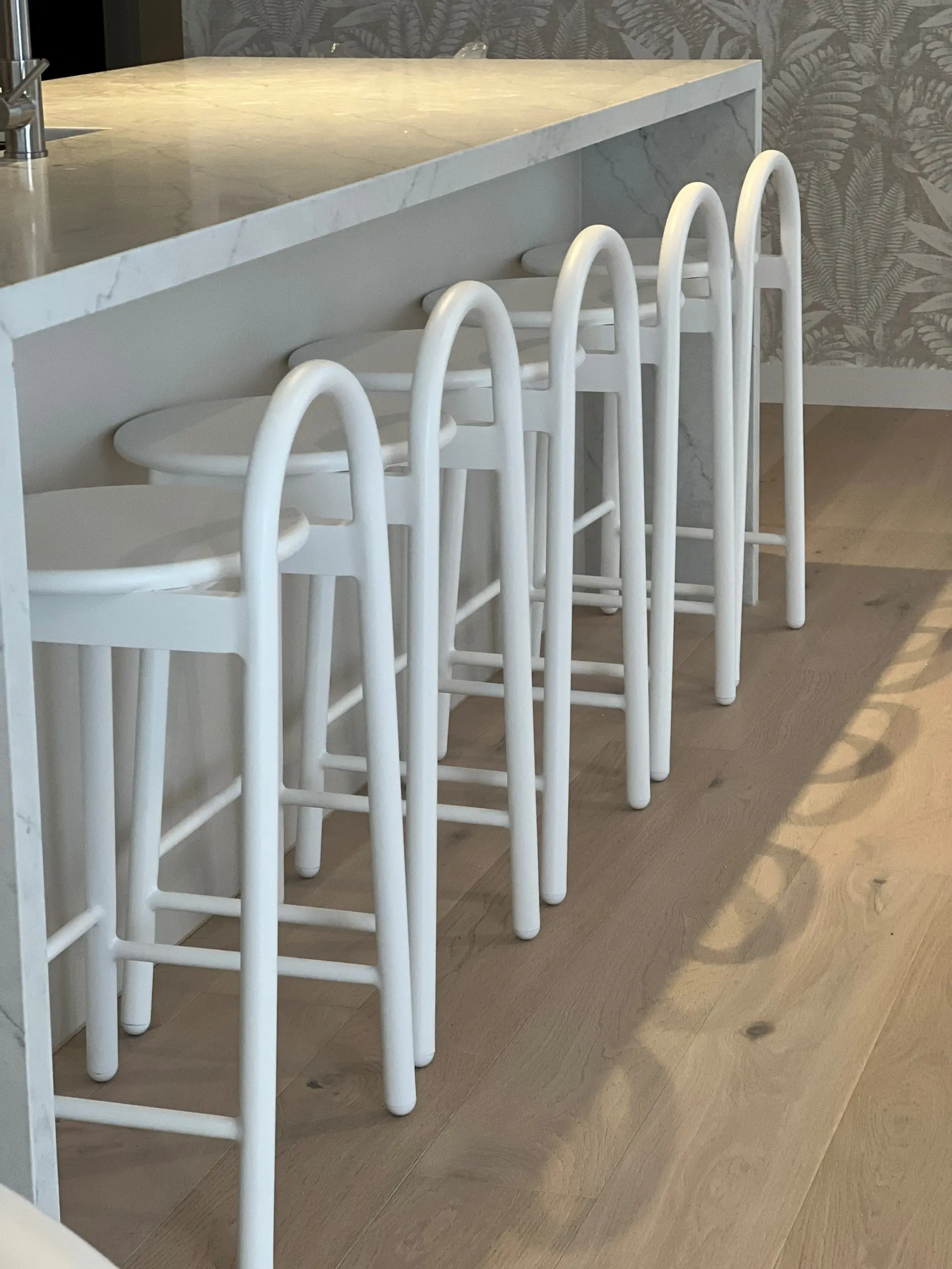 White arched bar stools along a marble waterfall island bench at Dawn Broadbeach, set against botanical wallpaper and oak flooring
