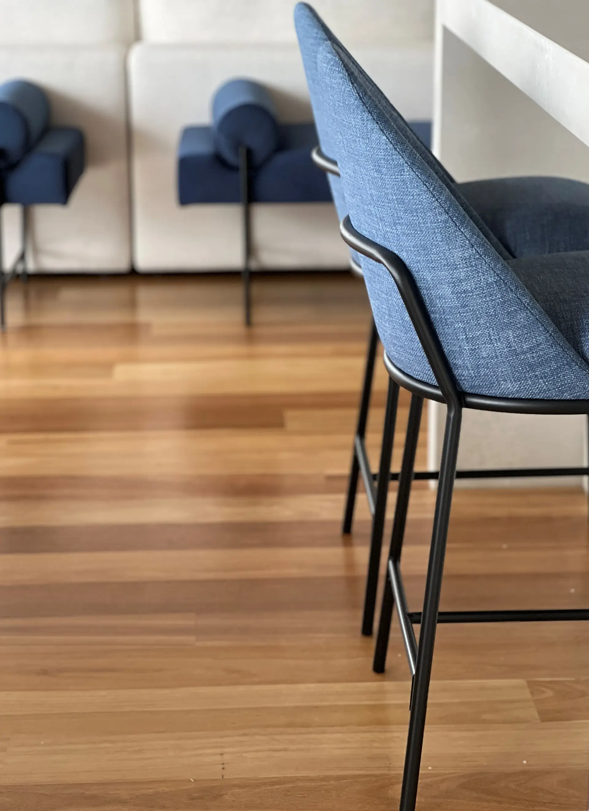 Blue upholstered bar stools at the kitchen island of the Mount Martha residence, with hardwood flooring and a lounge setting beyond