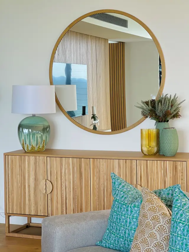 Fluted oak sideboard with round timber mirror, green glass lamp and turquoise cushions
