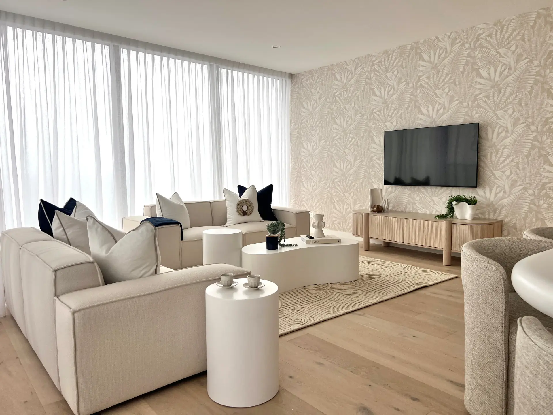 Living room at Dawn Broadbeach with cream modular sofas, a botanical wallpaper feature wall and a fluted timber media unit