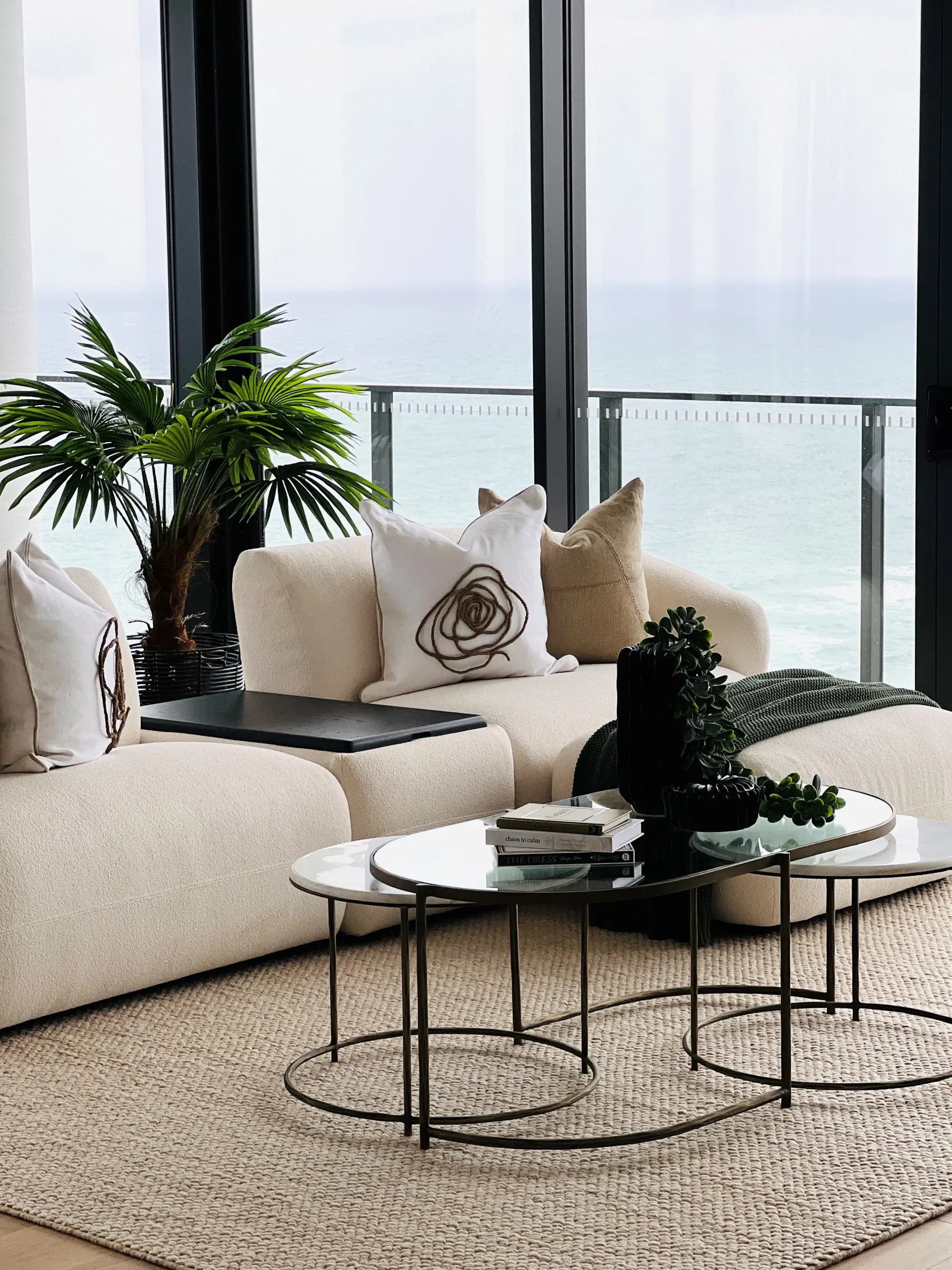 Living room at the Sandbar apartment with a cream bouclé modular sofa, jute rug and floor-to-ceiling glass framing an ocean view