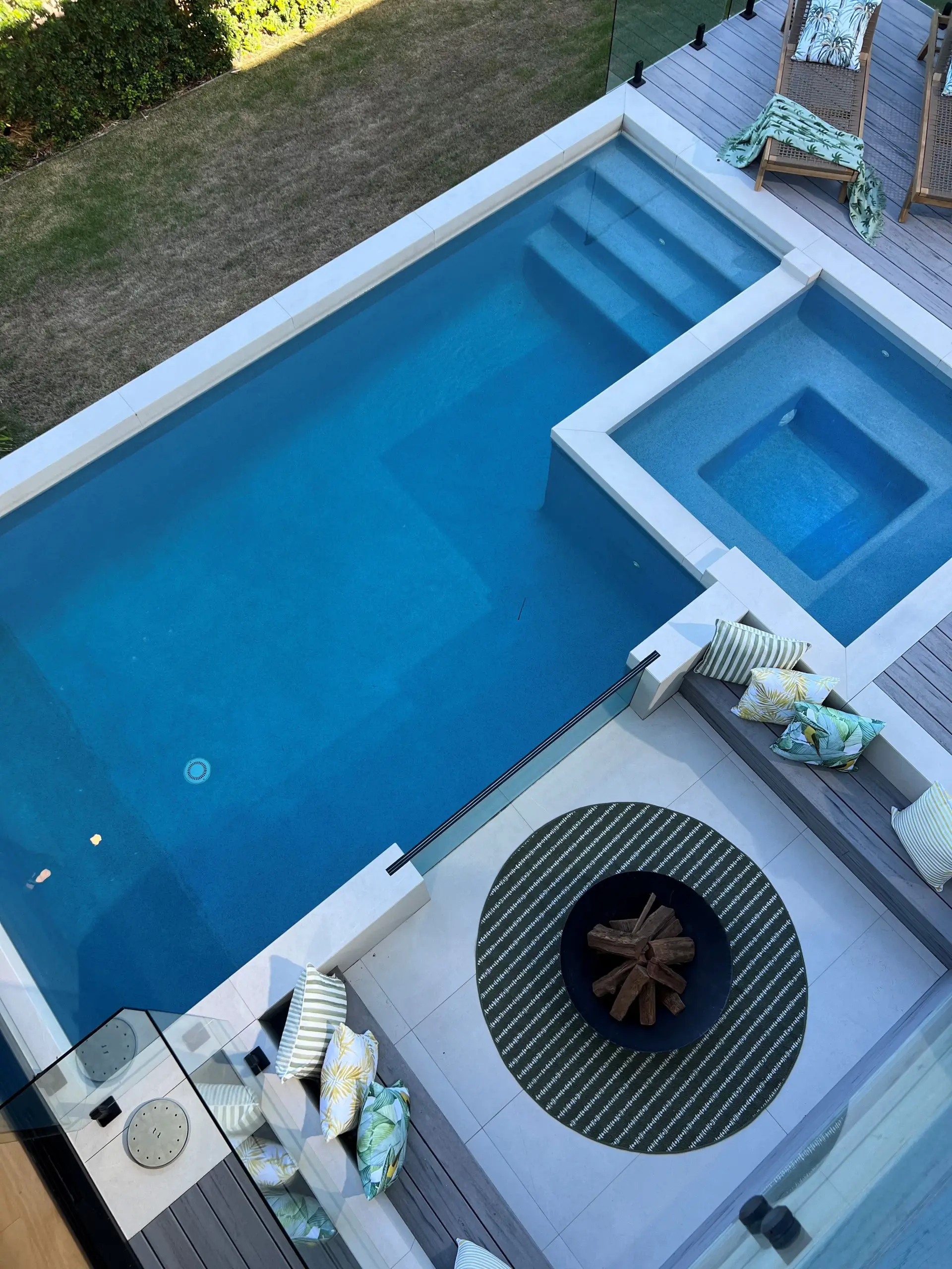 Overhead view of the Peregian Beach House pool and spa, with a timber deck, sun lounges, fire pit and tropical-print outdoor cushions