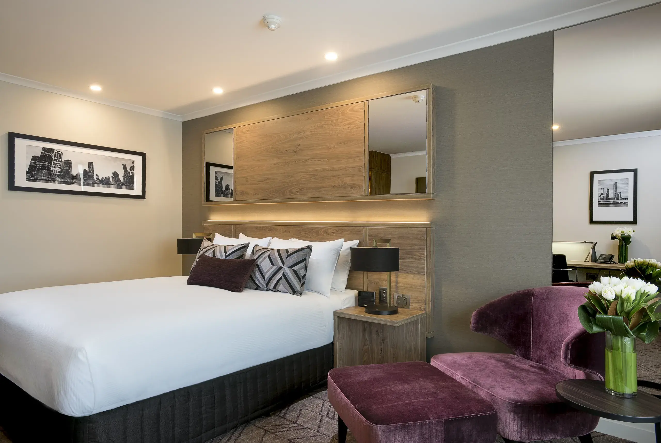 Rydges South Bank king guest room with timber-panelled headboard, integrated LED lighting and aubergine velvet armchair