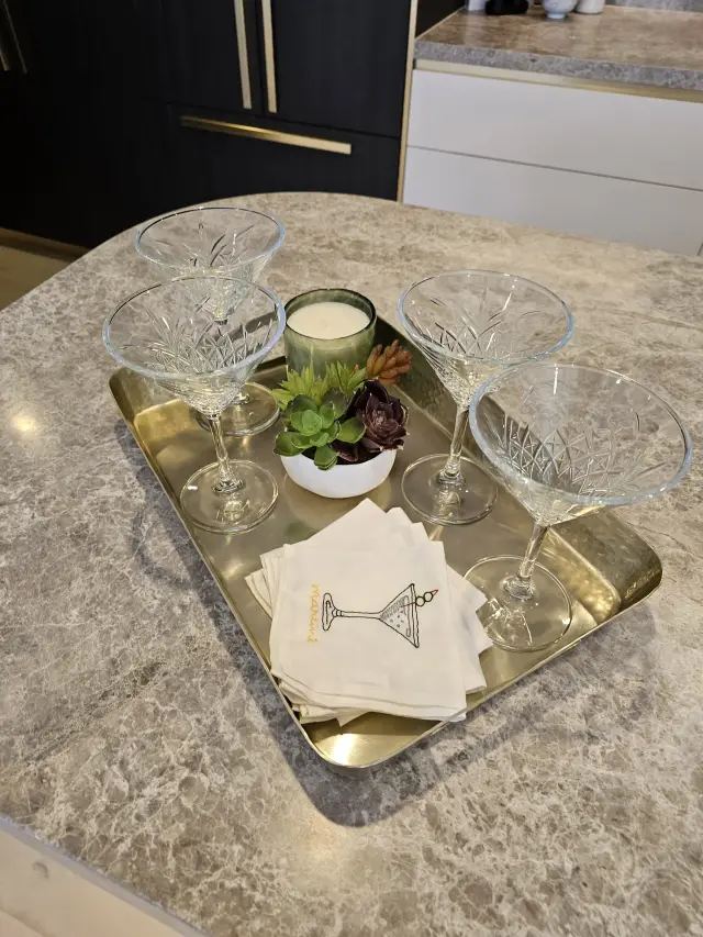 Gold tray of crystal martini glasses, candle and succulents on grey marble benchtop