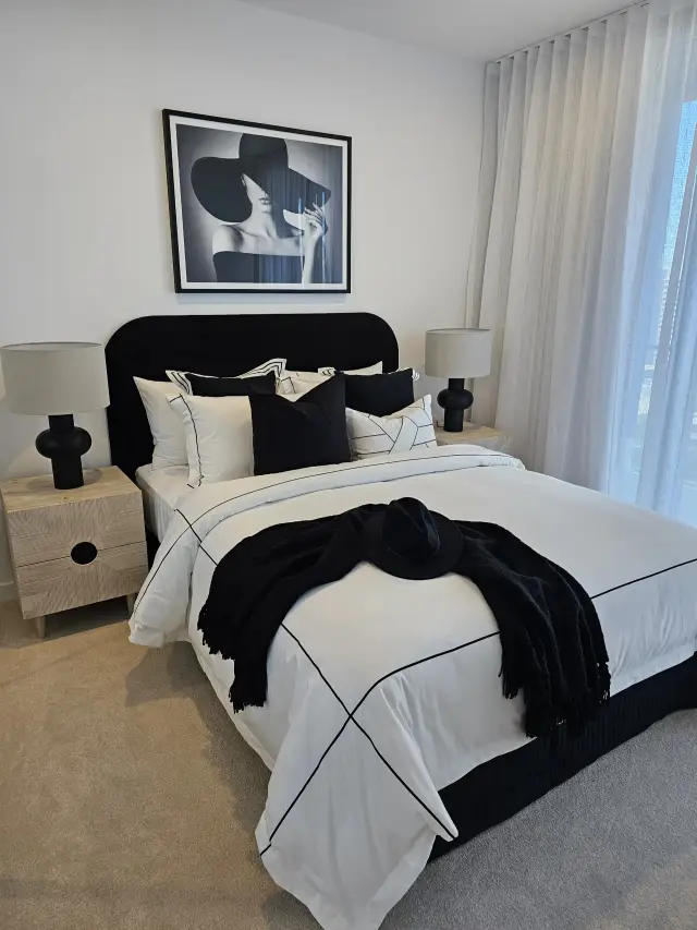 Master bedroom with black velvet bedhead, monochrome linen and woman-in-hat photography