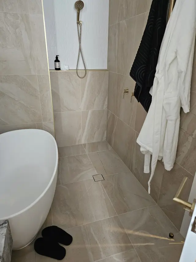 Ensuite with freestanding stone bath, brass rail shower and stone-look floor tiles