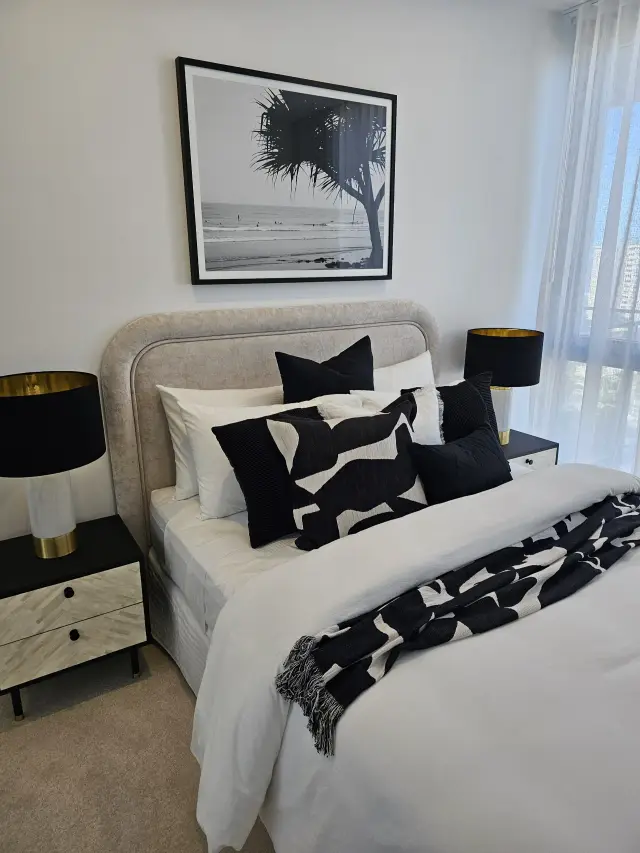 Bedroom with beige bedhead, black-and-white beach photograph and black-and-gold table lamps