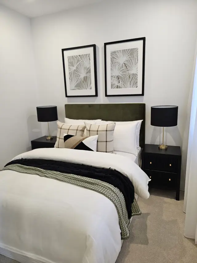 Guest bedroom with olive velvet bedhead, plaid cushions, black lamps and palm-frond prints